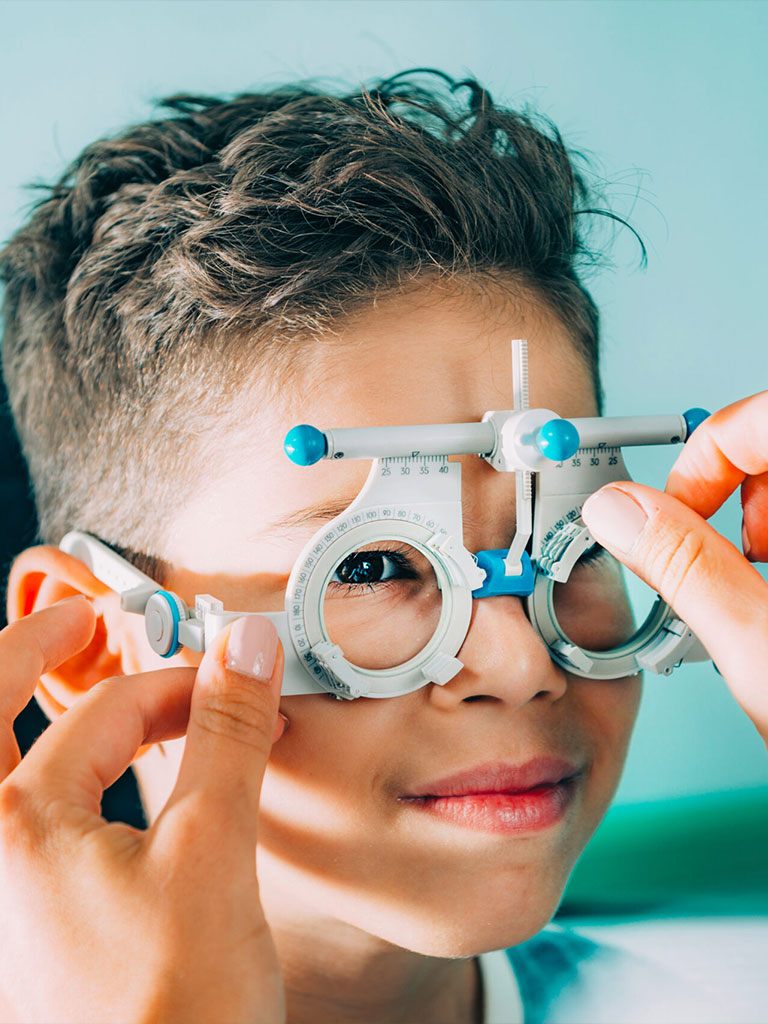 Ein Kind bei einer Augenuntersuchung, während ein Optiker ein Testbrillengestell anpasst