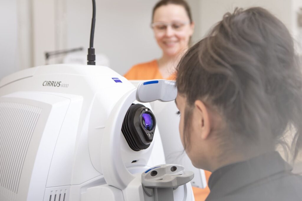 Untersuchung am OCT-Gerät: Patientin blickt in die Optik, Fachkraft im Hintergrund begleitet die augenärztliche Diagnostik.